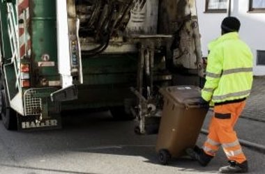 Müllmann fährt Mülltonne an Müllabfuhrfahrzeug