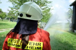 Feuerwehrfrau spritzt Wasser auf eine brennende Wiese