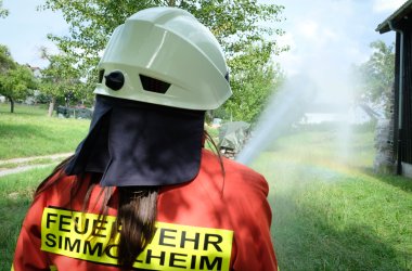 Feuerwehrfrau spritzt Wasser auf eine brennende Wiese