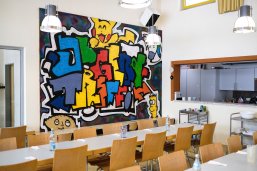 Blick auf das bunte Graffiti im Raum des Jugendtreffs, im Vordergrund stehen Tischreihen