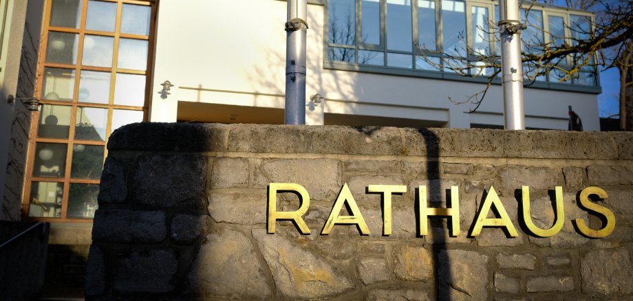 Schriftzug "Rathaus" auf einer Steinmauer, im Hintergrund ist der Sitzungssaal des Rathauses zu sehen Schriftzug "Rathaus" auf einer Steinmauer, im Hintergrund ist der Sitzungssaal des Rathauses zu sehen