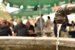 Brunnen im Vordergrund dahinter feiernde Menschen, die auf Bierbänken sitzen